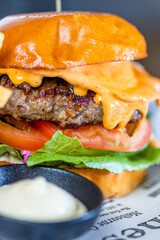 A hamburger with cheese, lettuce and tomato and a bowl of aioli sauce