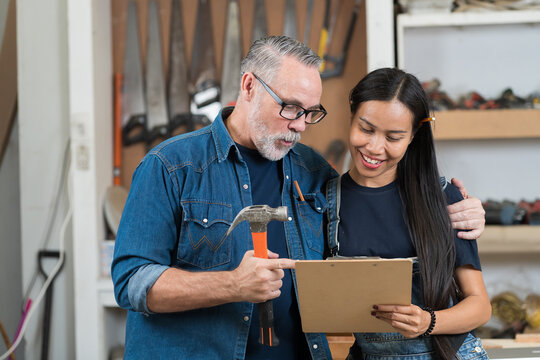 Portrait Of Happy Couple Carpenter Working Together In The Wood Workshop. Male And Female Carpenter Wear Uniform Working With At The Furniture Workshop