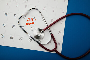 Doctor appointment reminder note on calendar with stethoscope, top view