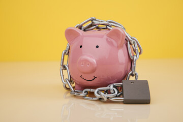 Piggy bank with chain and lock on yellow background