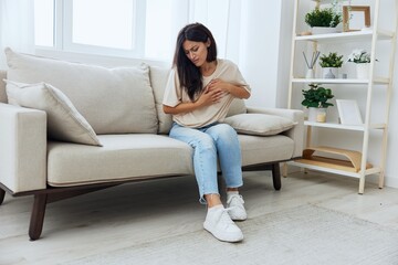 Woman sitting on sofa at home arm and shoulder pain, muscle sprain and joint pain, calcium problems in bones