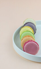 Multicolored macaroons in pastel shades on a white plate on a light pink background. Colorful macarons close up. Copy space. Macaroons creative, high key