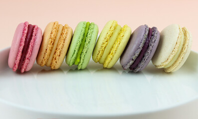 Multicolored macaroons in pastel shades on a white plate on a light pink background. Colorful...