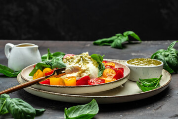 Salad with Tomatoes and Burrata cheese and green pesto on a dark background. banner, menu, recipe place for text, top view