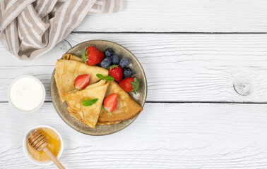 French crepes, pancakes or Russian bliny with strawberries, blueberries and mint on a white wooden...