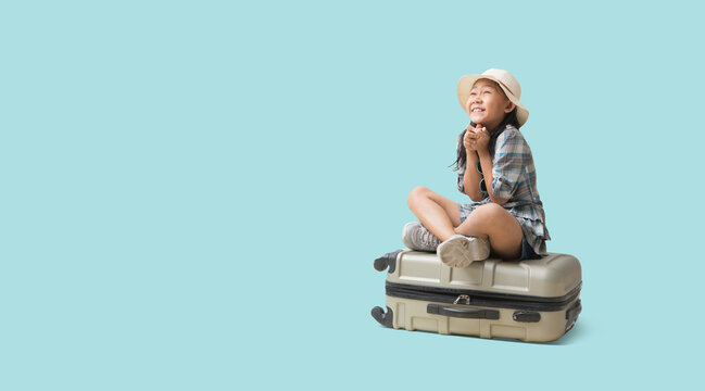 Happy Kid Travel Concept, Full Body Pretty Asian Little Girl Sits On A Suitcase Ready For Vacation Trip, Isolated On Pastel Plain Light Blue Background