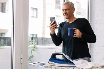 relaxed man having a break with the iron while looking at the phone and having a coffee