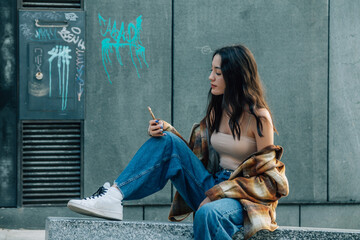 young girl sitting with phone on the street