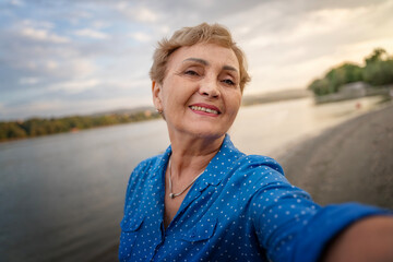 Beautiful happy mature elderly woman 60 years old takes a selfie on a smartphone outdoor