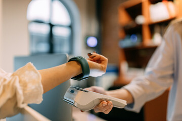 Female worker holding a paying machine, customer paying with a smart watch.