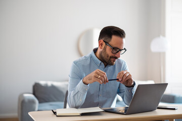 Businessman reading business tasks over the laptop, holding a pencil at the office.