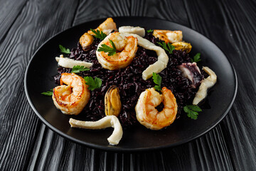 delicious black rice with shrimps and seafood on a black wooden rustic background