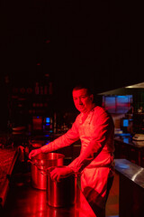 young caucasian chef-cook cut vegetables in kitchen. cook make vegetarian dish for restaurant visitors, man in white apron use sharp knife for better cuttingSideview portrait of a chef in neat uniform