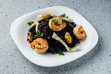 delicious black rice with shrimps and seafood on a gray stone background