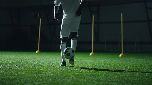 black football player kicking ball by feet, training in sport hall, closeup view of legs of sportsman