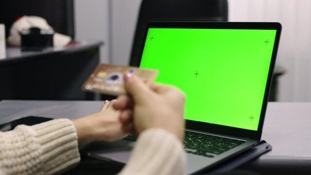 Over the shoulder shot of a business woman working in office interior on pc on desk, looking at green screen. Office person using laptop computer with laptop green screen, sitting at wooden table