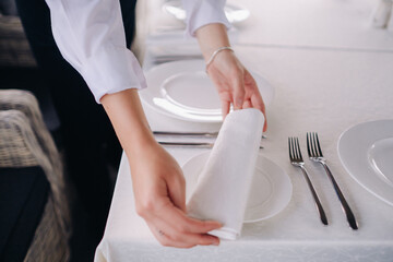 The waiter puts a white napkin on the plate. Beautiful table setting for a holiday without food - Powered by Adobe