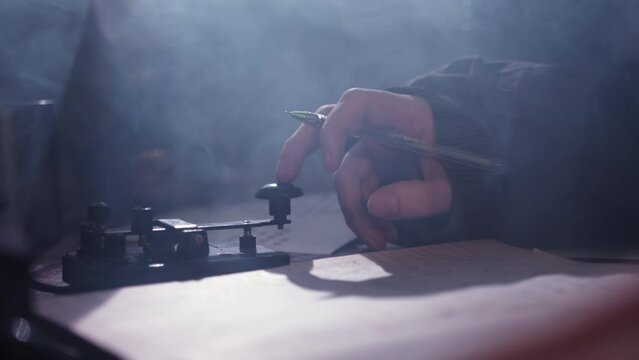 Man transmits information pushing button on telegraph in dark room filled with smoke. Finger of person tapping to communicate in Morse code closeup