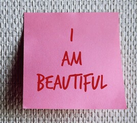 Pink note on wallpaper background with text I AM BEAUTIFUL, self-love affirmation to boost self-esteem, overcome negative thoughts, boost self acceptance and self respect