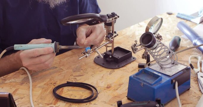 Electronics serviceman applying tin at micro switch contacts using soldering iron, close up