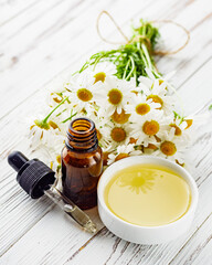 aromatic chamomile essential oil on a white wooden rustic background