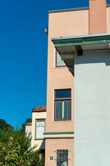 Building facade with white exterior wall and orange stucco with visible windows and front or back yard trees