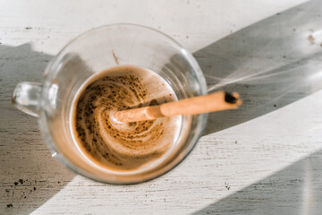 Top view of a glass mug with cappuccino coffee with a cinnamon stick.