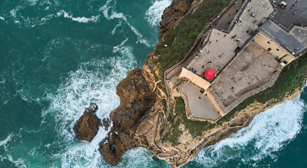Aerial view of an old lighthouse on a cliff with a fortress on the coast of the Atlantic ocean in...