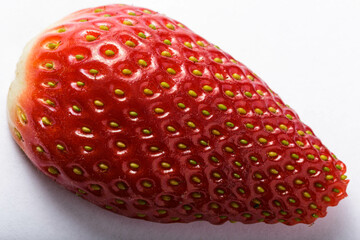 A whole strawberry on a white background, taken with a macro lens to showcase the fine details of the fruit's texture and shape. The bright red color of the strawberry stands out against the white 