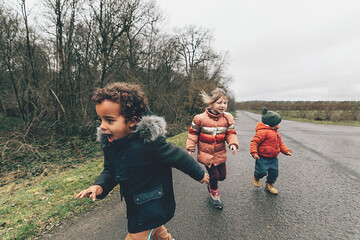 happy multiethnic children running on a road in the countryside in grey cold day