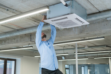 Caucasian bearded man repairing the air conditioner in the office. 