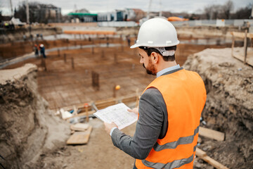 Back view of an engineer looking at blueprints on construction site.
