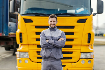 Portrait of a confident truck driver smiling at the camera while standing outdoors in front of the...