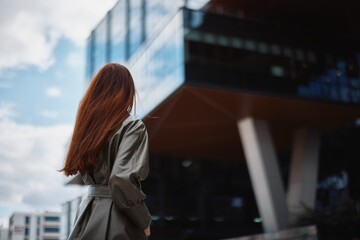 Young woman business talking on the phone with a smile and red hair in front of tall buildings in...
