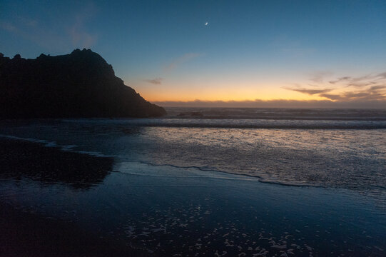 A crescent moon illuminates the beach, just after sunset, at Pfeiffer Beach. Big Sur, California.