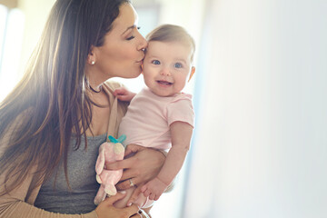 Mother, bonding and forehead kiss for baby girl on in house living room, nursery or family home bedroom in trust or love. Smile, happy and infant child with mom in support, security or safety comfort