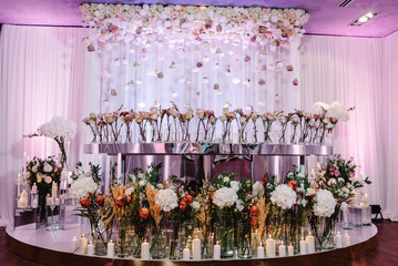 Arch and festive table newlyweds decorated with composition of flowers and greenery, candles in the banquet hall. Wedding decor on ceremony, party.