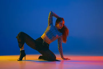 Gordijnen Passion. Portrait of young girl dancing high heel dance in stylish clothes over blue background in neon light. Concept of modern dance style © master1305