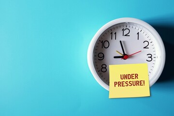 Clock on blue copy space background with note written UNDER PRESSURE! means dealing with time constraints which are often outside of control - difficulty task or having insufficient knowledge