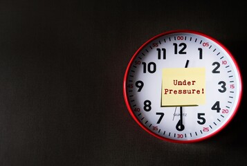 Clock on dark gray copy space background with note written UNDER PRESSURE! means dealing with time...