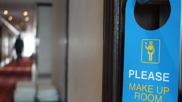 The cleaning sign is hang on the doorknob from the room in the hotel corridor where people walk