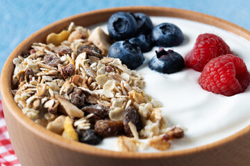 Yogurt with berries and muesli for breakfast in bowl on blue background. Close up
