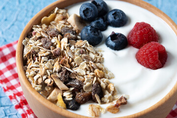 Yogurt with berries and muesli for breakfast in bowl on blue background. Close up