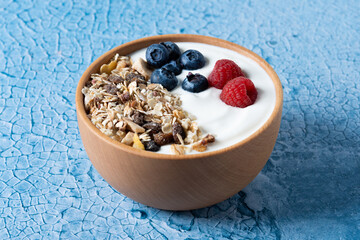 Yogurt with berries and muesli for breakfast in bowl on lbue background