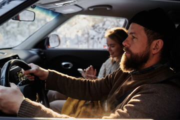 Serious bearded man concentrating on his driving, he sitting in car together with his girlfriend