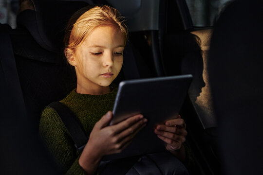 Little girl watching cartoons on digital tablet while sitting on backseat during trip by car