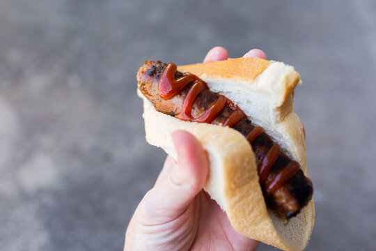 hand holding bbq sausage with sauce in white bread