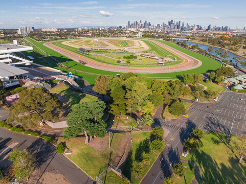 Aerial view of a horse racing track with carparking in front and a city skyline in the distance
