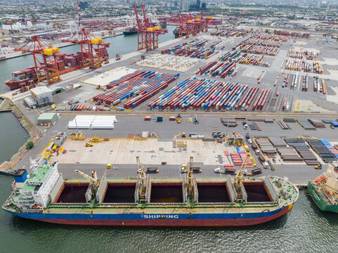 Aerial view of a cargo ship with its holds open at wharf lined with rows of containers