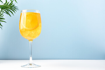 Orange drink with ice in glass on blue background. Refreshing tropical summer fruit lemonade or alcoholic drink with orange slice